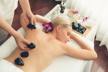 Lüks tatil köyündeki kaplıcalarda sıcak taş masajı. Gün ışığı sükunet ortamında, mutlu kadın müşteri bazalt taş masajından zevk alıyor. Rahatlatıcı bir sıcaklıkla vücudun üzerinde süzülüyor. Sessiz.