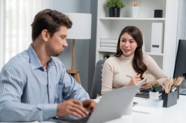 Akıllı yönetici dizüstü bilgisayarla yazarken iş analizi raporu için veri araştırma projesini modern ofis saatinde masa başında sorarak kadın iş arkadaşıyla konuşuyor. Varsayım.