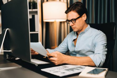 Akıllı iş adamı iş paragrafı dinamik pazarlama analizi planını analiz ediyor. Kağıt kağıtları ve bilgisayar monitörü raporlarını gece evdeki belge verileriyle karşılaştırmak için hazırlıyor. Bireysel.