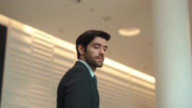 Profesyonel bir iş adamı kolları bağlıyken arkasını döner. Kafkasyalı mutlu yatırımcı, arka planı bulanık bir şekilde koridorda kollarını kavuştururken kameraya özgüvenle bakıyor. Portre. Sevinçli..