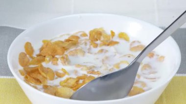 Kahvaltı için hazırlanmış sarı mısır gevreği ve sütle beyaz kasenin yan görüntüsü. Bir kaşık mısır gevreği ve sütlü tahıl almaya yaklaş. Makrografi. Sabah konseptinde sağlıklı yiyecekler. Pabulum.