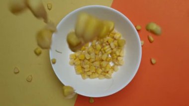 Sarı bir mısır tohumunun düşmesine ya da düşmesine yakın bir yere. Yukardan aşağıya mısır kabı ve ayrılmış sarı ve turuncu arka plan. Makrografi. Ağır çekim. Kahvaltıda. Pabulum.