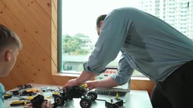 Yetenekli öğretmen, BTMM sınıfında araba modelini tamir eden genç öğrencilere yardım ediyor. Profesyonel eğitmen robot tamir makineleri dizüstü bilgisayar programlama sistemi ve kodlama komut ile masada. Öğretim