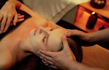 Beyaz kadın stres önleyici kafa masajı yapmaktan ve lüks otel veya otelde sıcak mum ışığında yüz güzelliği eğlencesi yapmaktan zevk alıyor. Sessiz.