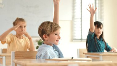 Sınıfta okuyan çeşitli çocuklarla çevrili beyaz bir çocuk öğretmenine soru sorup cevap verdiği için elini kaldırıyor. Mutlu öğrenci birlikte çalışıyor, oy veriyor, gönüllü oluyor, hocayı arıyor. Pedagoji.