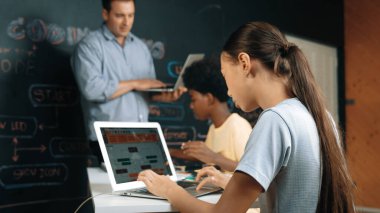 Afrikalı erkek manken tamir ederken beyaz kız programlama ya da kodlama sistemi. Öğretmen elinde dizüstü bilgisayar tutarken çeşitli çocukların web geliştirme programı yazmalarına bakıyor. Yenilik eğitimi. Öğretim.