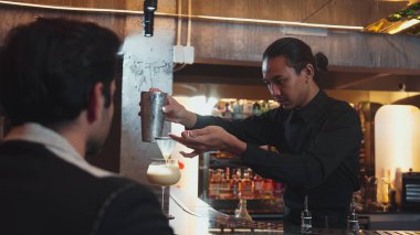 Asyalı akıllı barmen karışık kokteyl sallayarak lüks tezgah hazırlama servisine hazırlanıyor. Müşteri ön tarafındaki bara özel içki servisi yapıyor. Özel gece hayatı lüksü. Vinosity.