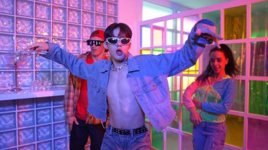 Asyalı adam gece kulübünde çeşitli neon ışıklarda dans ederken kolunu oynatıyor. Modern kulüpte çok kültürlü hippilerle dans eden şık elbiseli mutlu dansçı. Mutluluk.