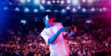 Yetişkinlerin elinde joystickle VR gözlükleri varken stadyumda arka planda bulanık oyunlar oynamaktan zevk alıyorlar. Afrikalı adam kontrol etmeyi ve artırılmış gerçeklik teknolojisini kullanmayı seviyor. Yaratıcılık.