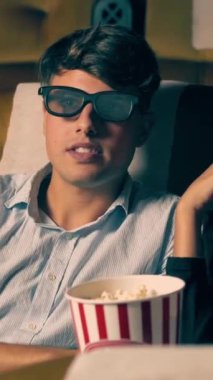 Sinemada üç boyutlu gözlüklü bir kadın ve erkek film izliyor. Ekrana bakar, heyecan verici ve patlamış mısır yer.