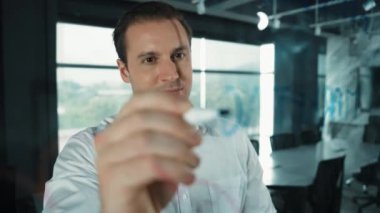 Akıllı iş adamı cam tahtanın önünde bir proje başlatmayı düşünüyor. Gülümseyen erkek proje yöneticisi yaratıcılık pazarlama stratejisini gösteren renkli yapışkan notlara bakıyor. Yönlendirici.