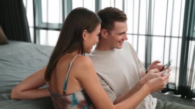 Genç çift, kredi kartıyla ödemek için internet üzerinden ödeme uygulaması ve dijital cüzdan kullanarak yatak odasında oturuyor. Mobil internet üzerinden alışveriş ve modern alımlar. Düzenle