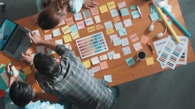 Gündelik kıyafet giyen, dizüstü bilgisayara bakan ve fikir paylaşan iş ekibinin zaman atlaması. Yapışkan notlar ve kulaklıkla masada çalışan ve renk paletini kontrol eden yöneticinin hava görüntüsü. Sempozyum.