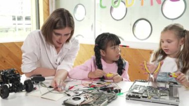 Yetenekli beyaz öğretmen öğrencilere dijital elektrikli aletleri öğretir ve açıklar. Uzman kız elektronik ekipman öğreniyor ve ana kartı cips ve kablolarla onarmak için kullanıyor. Etkinlik.