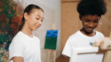 Resim dersinde erkek resim çizerken güzel bir kız tuvale benziyor. Çeşitli lise öğrencileri renkli duvarların önünde dikilirken çok kültürlü çocuklar yaratıcı faaliyetlere katılıyorlar. Öğretim.