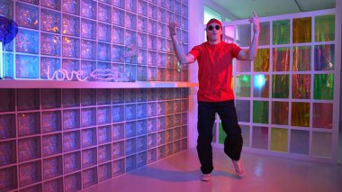 Komik break dansçı kameraya bakarken hiphop 'a doğru serbest adım atıyor. Çılgın mutlu hipster dans edip sokak dansı yaparken Led ışığında günlük kıyafet ve güneş gözlüğü takıyor. Mutluluk.