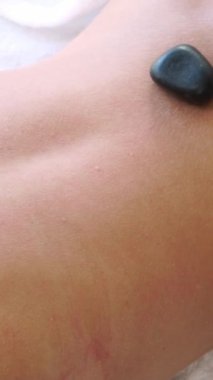 Kadın kaplıca salonunda profesyonel güzellik terapisti tarafından sıcak taş masajı görüyor. Lüks sağlık, sırt stresi ve gençleştirme kavramı..