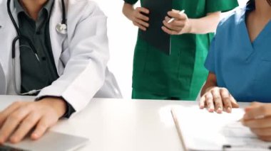 Hastane masasında birlikte çalışan ve tıbbi tedavi planlayan çeşitli profesyonel sağlık görevlileri. Takım çalışması başarılı hastalıklara ve hastalıklara yol açar. Ağır çekim. Katı.