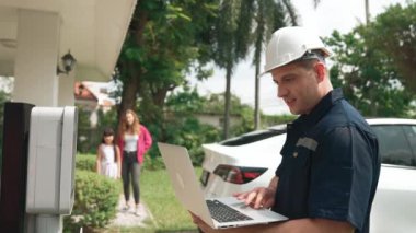 Evde EV şarj istasyonu kurulumu üzerinde çalışan nitelikli teknisyen, EV için dizüstü bilgisayarla şarj sisteminde sorun çıkarma ve yapılandırma ayarları yapıyor. Titiz