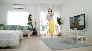 Beyaz anne ve Asyalı çocuk birlikte ev işi yapıyor ve müzik eşliğinde dans ediyorlar. Çekici anne ve kız modern yatak odasını temizlerken şarkı söyleyip rahatlatıcı müziğe atlıyorlar. Yaşam tarzı. Pedagoji.
