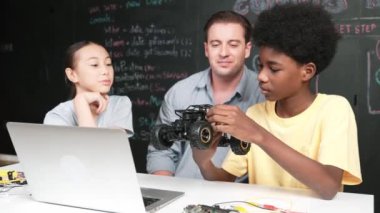 Afrikalı çocuk araba modelini dizüstü bilgisayar ve kabloyla incelerken öğretmen de karatahtadaki robotik yapıyı şifreli ya da STEM sınıfında hızlı bir şekilde açıklıyor. Eğitim. Öğretim