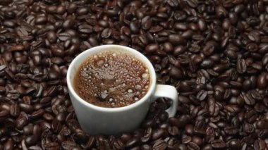Taze espresso beyaz fincana kahve çekirdeği yığını ile dolduruldu. Kahverengi arkaplanlı fincana koyu kahve dökmek ve tohumları ahşap masaya saçılmak. Kapatın. Üst Manzara. Geliştirilebilir.