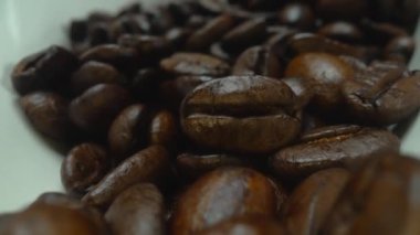 Makro kahve çekirdekleri kamerayla kaşığa saçılıyor. Beyaz kaşık kepçesiyle kahverengi kahve çekirdeklerini kapayın ve siyah arkaplanla dağılın. Kafein enerji içeceği konsepti. Pabulum.