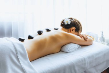 Lüks tatil köyündeki kaplıcalarda sıcak taş masajı. Gün ışığı sükunet ortamında, mutlu kadın müşteri bazalt taş masajından zevk alıyor. Rahatlatıcı bir sıcaklıkla vücudun üzerinde süzülüyor. Sessiz.