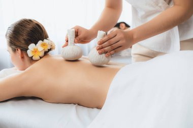 Sıcak bitkisel top spa masaj vücut tedavisi, masör nazikçe bitki torbasını çift müşteri vücuduna bastırıyor. Aromaterapi dinlenme sükuneti ve sükuneti kaplıca salonundaki atmosferi aydınlatıyor. Sessiz.