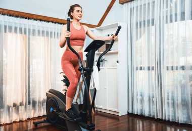 Spor ve atletik bir kadın, evdeki fiziğe ve sağlıklı spor yaşam tarzına uygun vücut egzersizi sırasında eliptik koşu makinesiyle koşuyor. Gaiety evde egzersiz eğitimi.