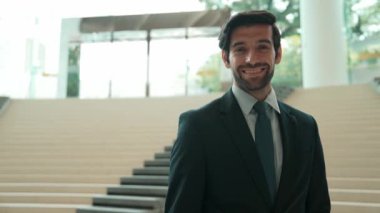 Akıllı iş adamı merdivenlerde kameraya bakıyor. İş elbisesi giyerken kameraya gülümseyen başarılı adamın yakın çekimi. Yönetici, kameraya bak. Hareket eden kamera. Sevinçli..