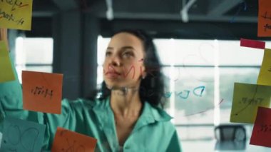 Zeki, profesyonel İspanyol iş kadınının portresi renkli yapışkan notlarla cam tahtaya pazarlama fikirleri yazıyor. Genç yönetici, analiz iş planının zihin haritasını çiziyor. - Yakın çekim. Yönlendirici.