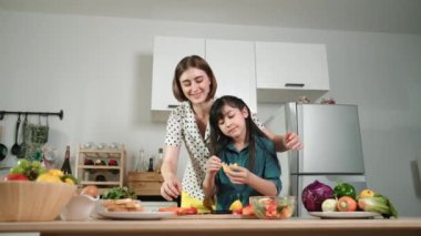 Zeki beyaz anne ve Asyalı kız birlikte yemek pişiriyor ve sebze doğruyor ya da akşam yemeği için salata hazırlıyor. Mutlu anne ve kız taze yemekle sağlıklı yemek yapıyorlar. Eğitim konsepti. Pedagoji.