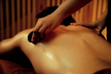 Sıcak mum ışığıyla lüks bir tatil köyündeki kaplıca salonunda sıcak taş masajı, mutlu erkek müşteri bazalt taşı masajının keyfini çıkarırken rahatlatıcı bir sıcaklıkla vücudun üzerinde süzülüyor. Sessiz.