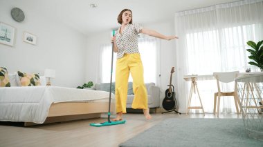 Modern apartman dairesinde dans ederken yerleri paspaslayan beyaz bir hizmetçi. Mutlu enerjik anne ya da temizlikçi müzik eşliğinde oturma odasını temizlemekten zevk alır. Yaşam tarzı. Pedagoji.