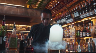 Asyalı barmen dumanlı klasik karışık viski kokteyli sunumu yapıyor. Harika bir sunum. İçecek tezgahı lüksünde özel, lezzetli, yaratıcı bir reklam içeceği öneriyor. Vinosity.