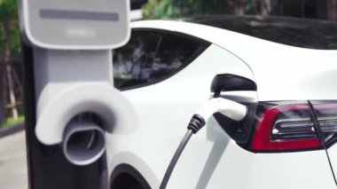 Yavaş çekim EV elektrikli araba yazın yeşil sürdürülebilir şehir parkı bahçesinde şarj oluyor. Elektrikli araç iç organları için kentsel yaşam tarzında sürdürülebilir temiz şarj edilebilir enerji