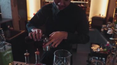 Güzel görünümlü Asyalı barmen içki şurubunu kullanarak lüks içki tezgahında cam hazırlama, gece kulübü lüksündeki düzgün profesyonel barmen kostümü yapıyor. Vinosity.