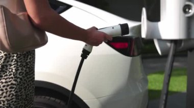Genç bir kadın, yeşil sürdürülebilir şehir parkı bahçesinde elektrik yüklü EV arabasıyla geziyor. Sürdürülebilir kentsel yaşam tarzında, yeniden şarj edilebilir elektrikli araç iç organlarıyla alışveriş yapmak için.