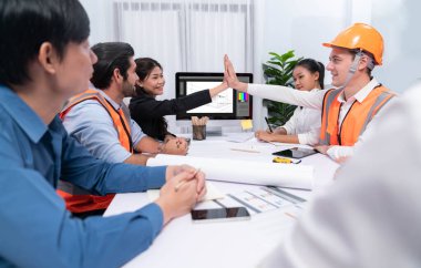 Çeşitli inşaat mühendisi ve müvekkil grupları, mimari proje üzerinde başarılı bir anlaşma yaptıktan, inşaat planını gözden geçirdikten ve toplantı masasında plan oluşturduktan sonra kutlama ve beşlik çakışma yaptılar.