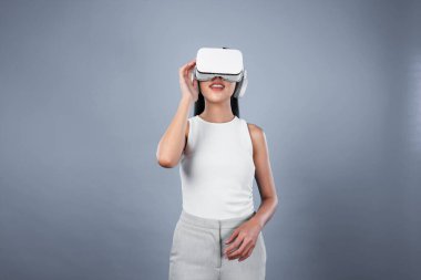 Gri arka planı olan zeki bir kadın metaevrene bağlı VR kulaklık takıyor, gelecekçi siber uzay topluluğu teknolojisi. Zarif bir kadın sanal bir manzara gördüğü için heyecanlı. Halüsinasyon.