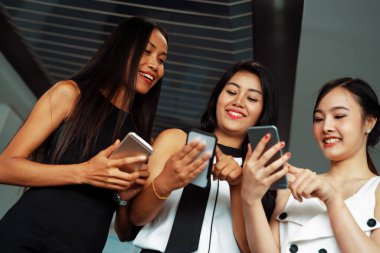 Üç kadın arkadaş ellerinde cep telefonuyla sohbet ediyorlar. Sosyal medya, dedikodu haberleri ve online alışveriş kavramı. uds