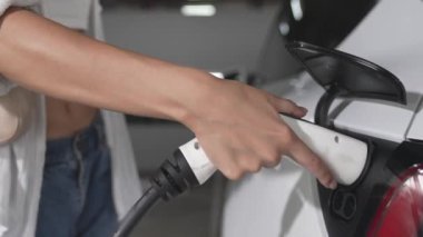 Yavaş çekim kadın, EV elektrikli arabasıyla şehir merkezindeki alışveriş merkezinin otoparkına gidiyor. Sürdürülebilirlik yaşam tarzını yeşil, temiz, yeniden şarj edilebilir elektrikli araç iç organlarıyla şarj ediyor.