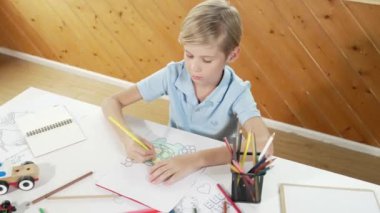 Yaratıcı resim boyayan ve sanat dersinde okuyan mutlu çocuk. Sevimli beyaz çocuk çevrimiçi test yaratıcı öğrenme eğitiminde renklendirme kitabı öğrenmekten zevk alıyor ya da heyecan duyuyor. Üst Manzara. Etkinlik.