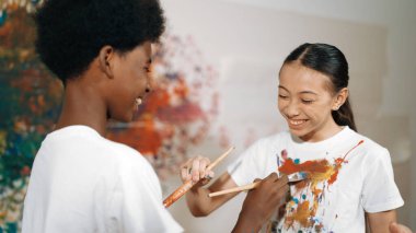 Resim dersinde, renkli duvarda, boyalı beyaz gömlekleri boyayarak gülümseyen farklı çocuklar. Tecrübe alışverişini temsil etmek, birbirimizi öğrenmek. Öğretim.