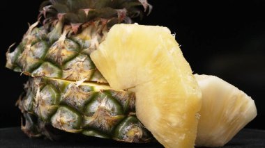 Taze ananaslı ve ayrı siyah arkaplanlı bir ananas dilimli videoyu kapat. Kaba ve balmumu kabuğu, dikenli yeşil yapraklardan bir taç, yemek fotoğrafçılığı. Geliştirilebilir.