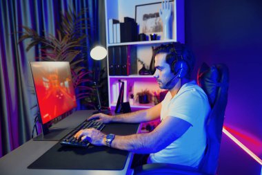 Kulaklık takan akıllı oyun flaması hafta sonu neon dijital siber ışıklandırma odasında son yaşam tarzı yarışmasında şampiyon olmak için bilgisayar ekranında araba yarışı oynamaktan zevk alır. Tahmin et..