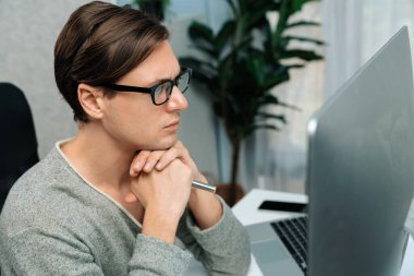 Modern ofiste oturan akıllı bir ofis çalışanı, ciddi bir yüz ifadesi olan, güzel görünümlü gözlük takan bir kamera. Yeni bir profil üzerinde sıradan bir günde çalışan iş adamı kavramı. Bireysel.