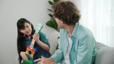 Akıllı kız oturma odasında ukulele çalarken beyaz bir babanın motivasyona ve teşviğe el çırpması. Amerikalı kız babasına gösterirken gitar öğreniyor. Aile yaratma kavramı. Pedagoji..