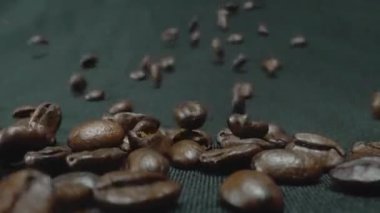 Kavrulmuş kahve çekirdeklerini yakın plan siyah arkaplan ile raylarda yuvarlanıyorlar. Makro kahve çekirdeği düşüyor ve siyah arka planla kamerayı örtüyor. Kafein konsepti. Pabulum.